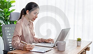 Young asian enthusiastic businesswoman at modern office desk with laptop.