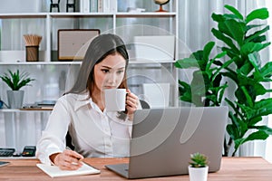 Young asian enthusiastic businesswoman at modern office desk with laptop.