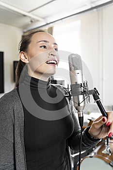 Young Asian or European woman singing to microphone in music or radio studio