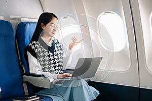 Young Asian executive excels in first class, multitasking with digital tablet, laptop and smartphone. Travel in style, work with