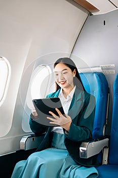 Young Asian executive excels in first class, multitasking with digital tablet, laptop and smartphone. Travel in style, work with