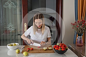 Young caucasian woman cooking fresh fruit and vegetable salad on table. Person preparing healthy yummy eating lunch in