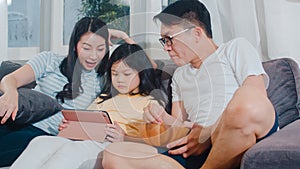 Young Asian family and daughter happy using tablet at home. Japanese mother, father relax with little girl watching movie lying on