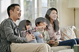 young asian family with two children watching tv together at home