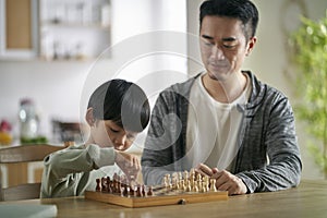 young asian father playing chess with son at home