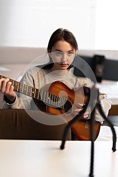 Young asian female artist blogger playing on guitar shooting music video or tutorial on smartphone at home studio