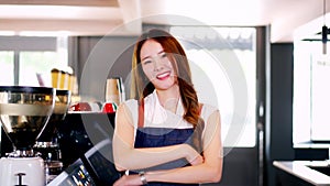 Young Asian female barista in apron having arms folded and smiling while looking at camera in the coffee shop