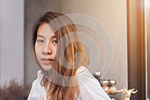 Young Asian female barista relaxing by sitting in her own coffee shop and be warmed by the warm sunshine in late of afternoon.