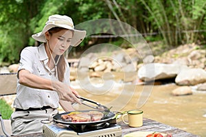 Young Asian female camping in the forest campground, enjoy making a pork chop steak