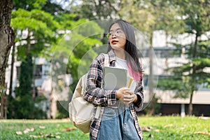 A young Asian female college student carrying a backpack and stuff, standing in the campus park