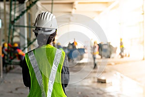 Young Asian female construction engineer wearing a hat and a green safety vest, stands looking at work in the construction zone