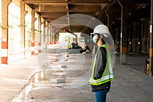 Young Asian female construction engineer wearing a hat and a green safety vest, wearing a hat and a green safety vest, stands