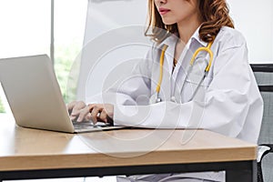 Young Asian female doctor using computer laptop on the desk in hospital office.