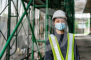 Young Asian female engineer wearing a medical mask to cover her mouth and wearing a white safety helmet Hand holding paper,