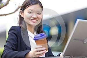 Young Asian female executive drinking coffee and using laptop PC