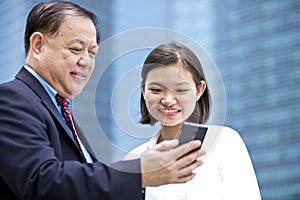 Young Asian female executive and senior businessman using smart phone