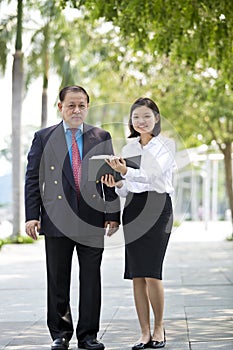 Young Asian female executive and senior businessman walking together