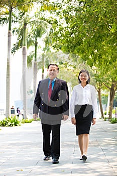 Young Asian female executive and senior businessman walking together