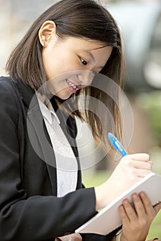 Young Asian female executive writing on notepad
