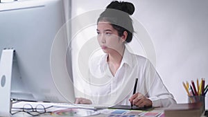 Young Asian female freelance graphic designer or artist retoucher drawing on a digital tablet with a stylus pen