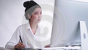 Young Asian female freelance graphic designer or artist retoucher drawing on a digital tablet with a stylus pen