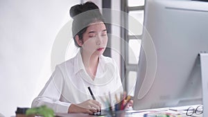 Young Asian female freelance graphic designer or artist retoucher drawing on a digital tablet with a stylus pen