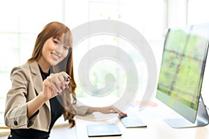 Young Asian female graphic designer sitting on the desk with computer and drawing something while smiling, copy space for the