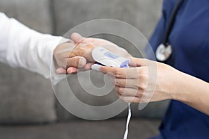 young asian female nurse measuring pulse with oximeter to a senior woman at home