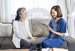 young asian female nurse in uniform visiting a senior patient at home