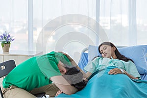 Young Asian female patient look at male relative patient or husband touching his sholder while sleeping for taking care, stand by photo