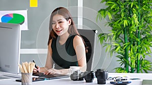 Young asian female photographer sitting in her studio, looking at camera  and focusing on retouching and editing photos by using