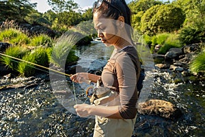 A young asian female standing fly fishing in a riffle on a river