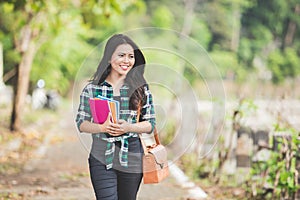 Young asian female student holding books while walking on the pa