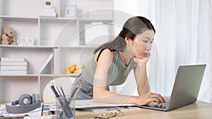 Young Asian female student watching teacher's live performance or video call on laptop in classroom at home