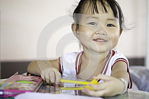 A young Asian female toddler with black hair is smiling and showing beautiful teeth. She happily with Colored pencils. And copy sp