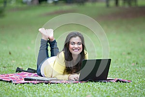 Young asian female university or college student lying on stomach in park