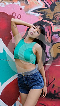 Young Asian female wears denim shorts and cropped top in front of street art