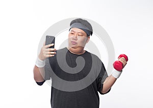 Young Asian funny fat sport man exercise with dumbbell and using smartphone isolated on white background.