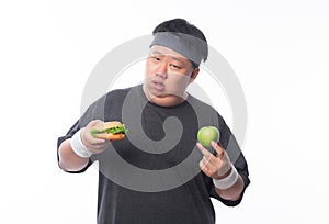 Young Asian funny fat sport man holding hamburger and green apple isolated on white background. Healthy lifestyle concept.