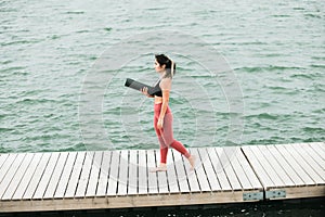 Young asian girl doing yoga outdoors on the pier by the lake