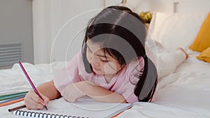 Young Asian girl drawing at home. Asia japanese woman child kid relax rest fun happy draw cartoon in sketchbook before sleep lying