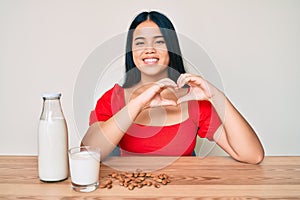 Young asian girl drinking healthy almond milk smiling in love doing heart symbol shape with hands