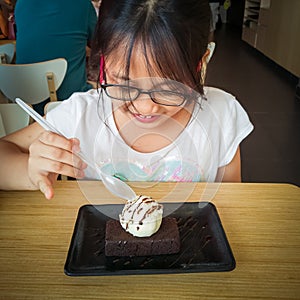 A young asian girl enjoying Brownie with vanilla ice cream served on a plate at a restaurant