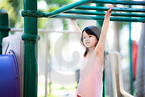Young Asian girl hanging on monkey green bars in playground. Summer outdoor activity for child.