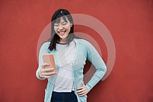 Young asian girl having fun using mobile phone outdoor - Focus on face