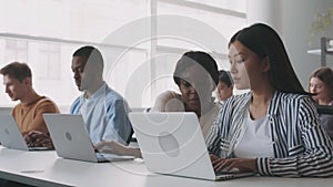 Young asian girl having troubles during lesson, asking her black groupmate for help, typing on laptops at college