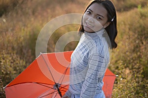 Young Asian girl hold umbrella wear jean and sweater standing at field grass sunset time