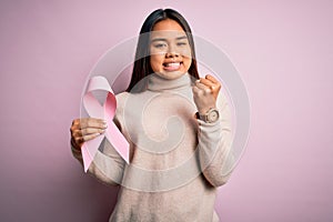 Young asian girl holding pink cancer ribbon symbol for suppport over isolated background annoyed and frustrated shouting with