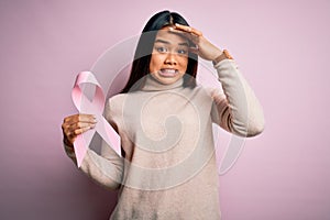 Young asian girl holding pink cancer ribbon symbol for suppport over isolated background stressed with hand on head, shocked with