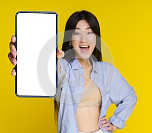 Young asian girl holding smartphone in hand showing white screen for your mock up mobile app advertisement and excited